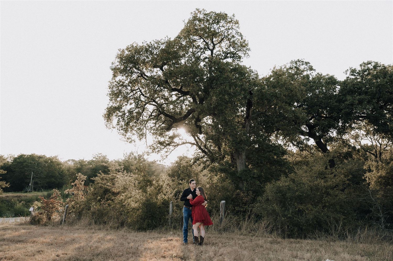 A silhouetted couple stands beneath a majestic tree during sunset in a natural outdoor setting.