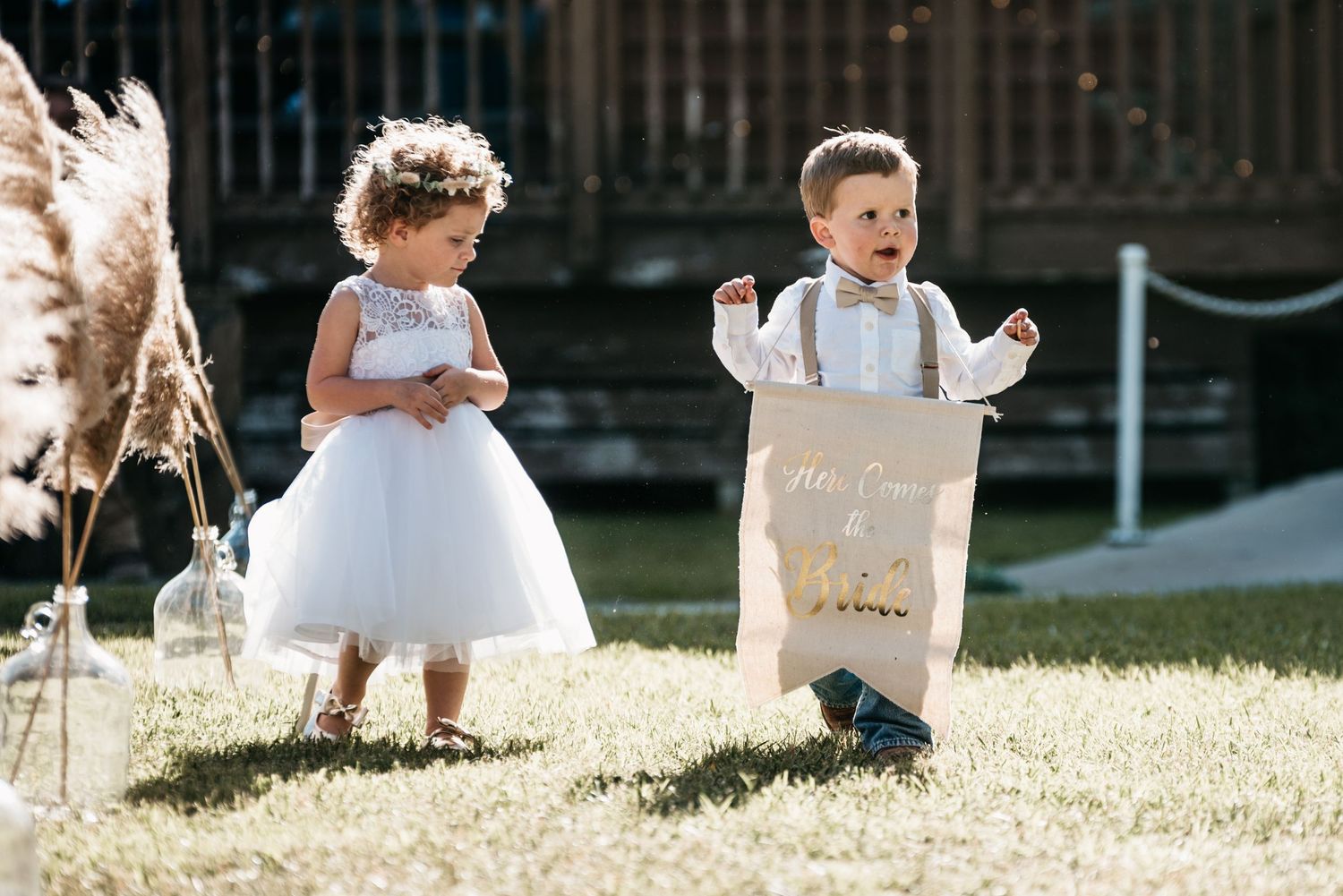 Two children in formal attire playing on grass during a wedding celebration.