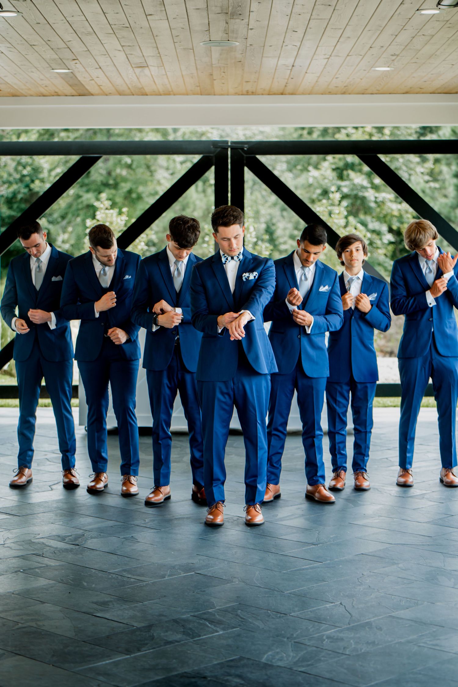 Groomsmen in matching navy suits show off their dress shoes in creative photo pose.