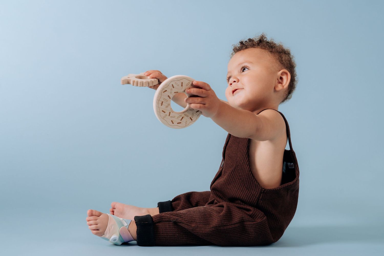 Small child in brown outfit holding medical device while sitting.