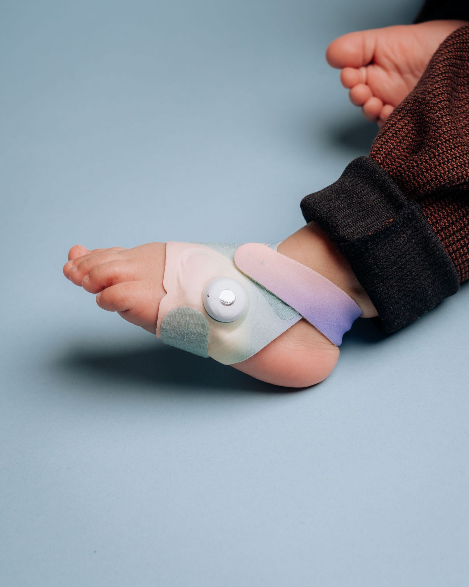 Medical foot brace with purple and white straps attached to small foot against blue background.
