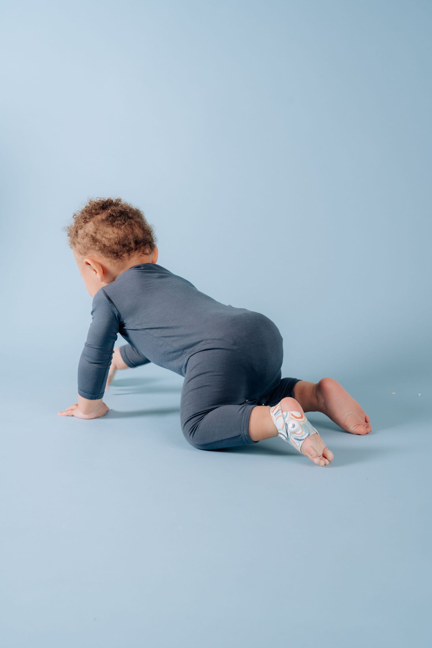 Child in gray outfit crawling on blue studio background.