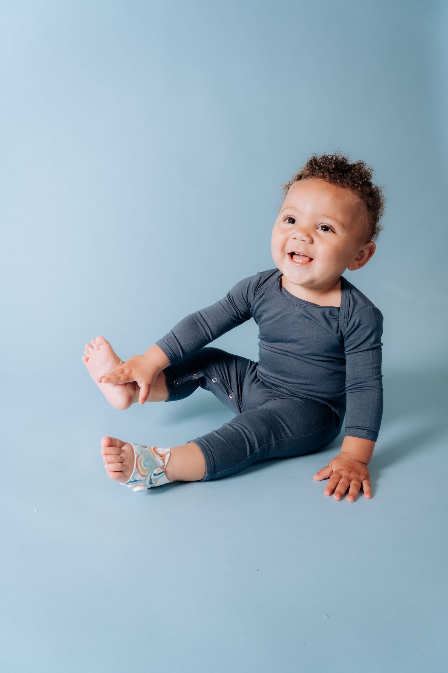 Small child wearing gray outfit sitting on blue backdrop.
