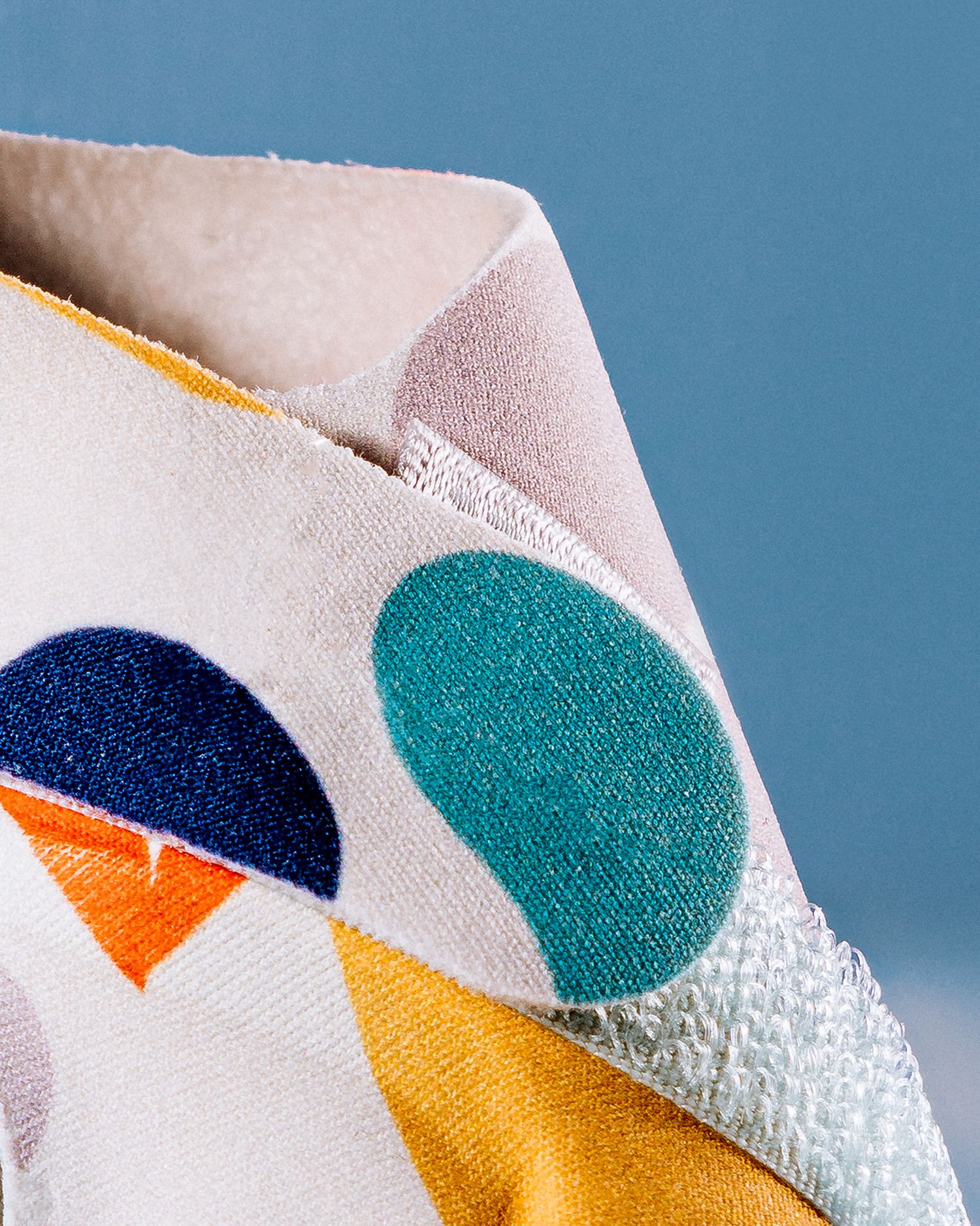 Close-up of fabric with colorful geometric circles in navy, teal, orange and yellow against a light background.