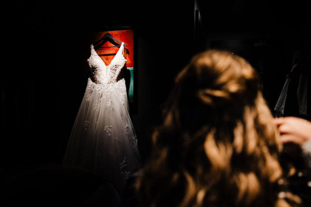 Wedding dress hangs illuminated in red light against dark background.