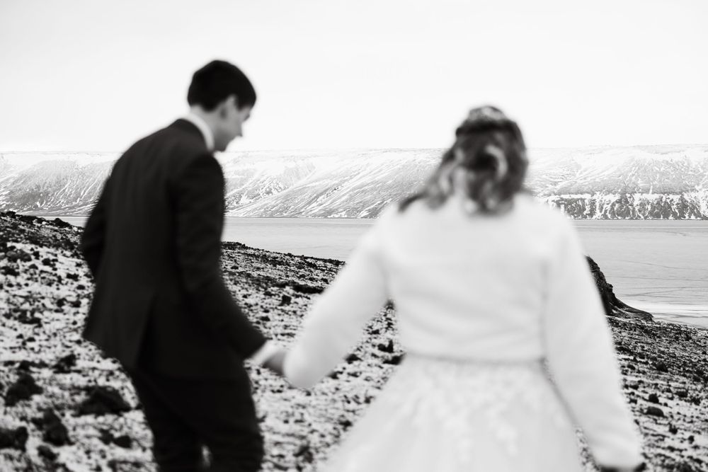 Black and white photo of a wedding couple walking along a scenic beach.