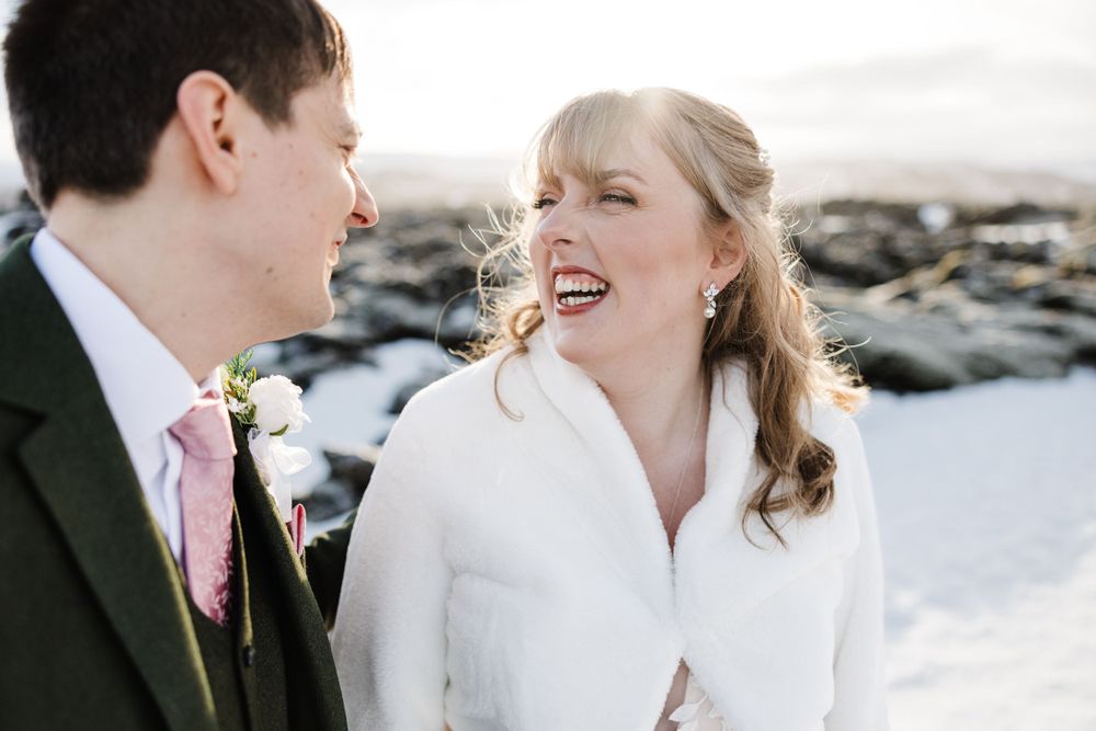Candid moment between newlyweds on snowy terrain with winter mountains behind them.