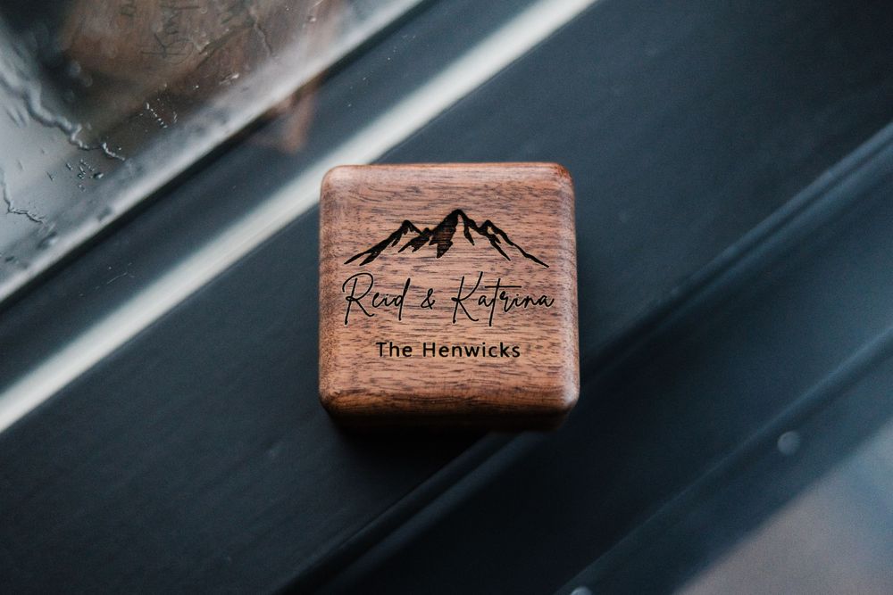 Wooden ring box with mountain logo and text reading 'The Henricks' engraved on the surface.