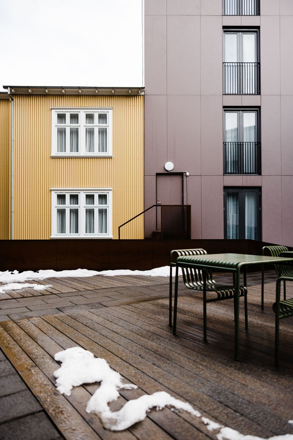 Contrast between yellow and gray buildings with outdoor furniture and snow patches on wooden deck.