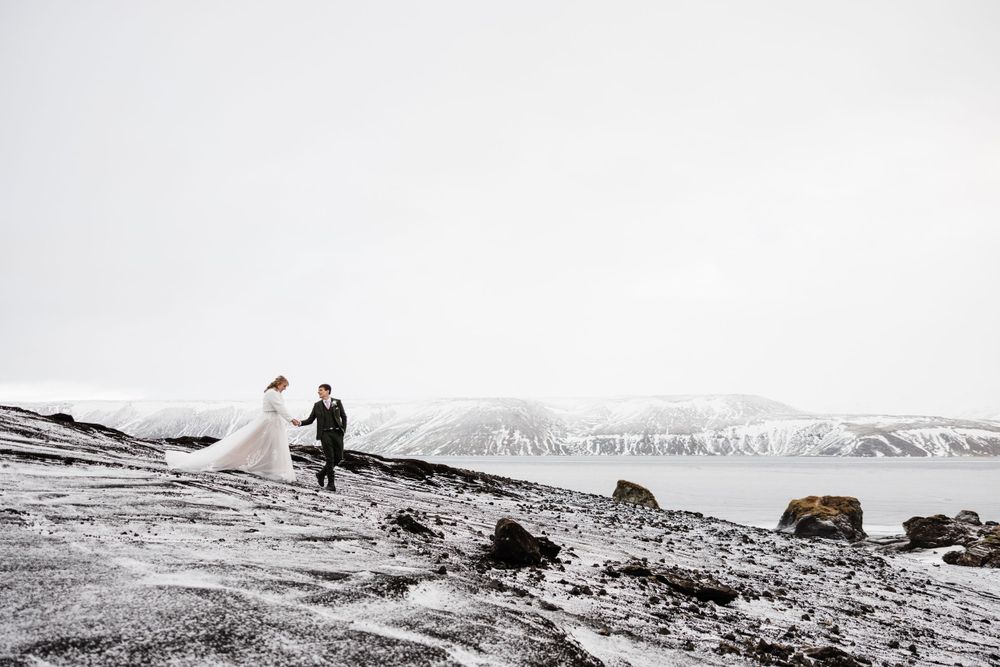 Distant view of wedding couple on hillside with mountain landscape in monochromatic tones.
