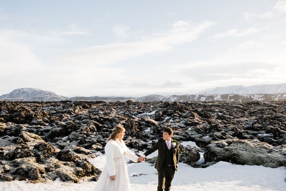 Wedding couple walking through dramatic snow-covered volcanic landscape.