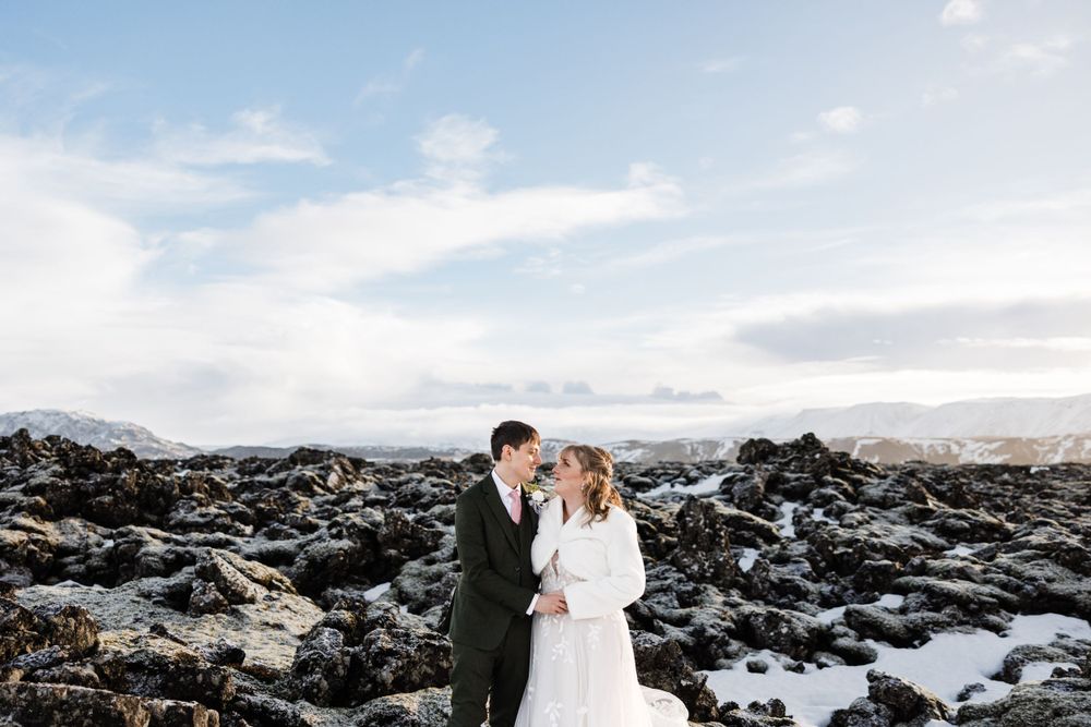Wedding couple standing together against snowy rocky landscape with mountains in background.