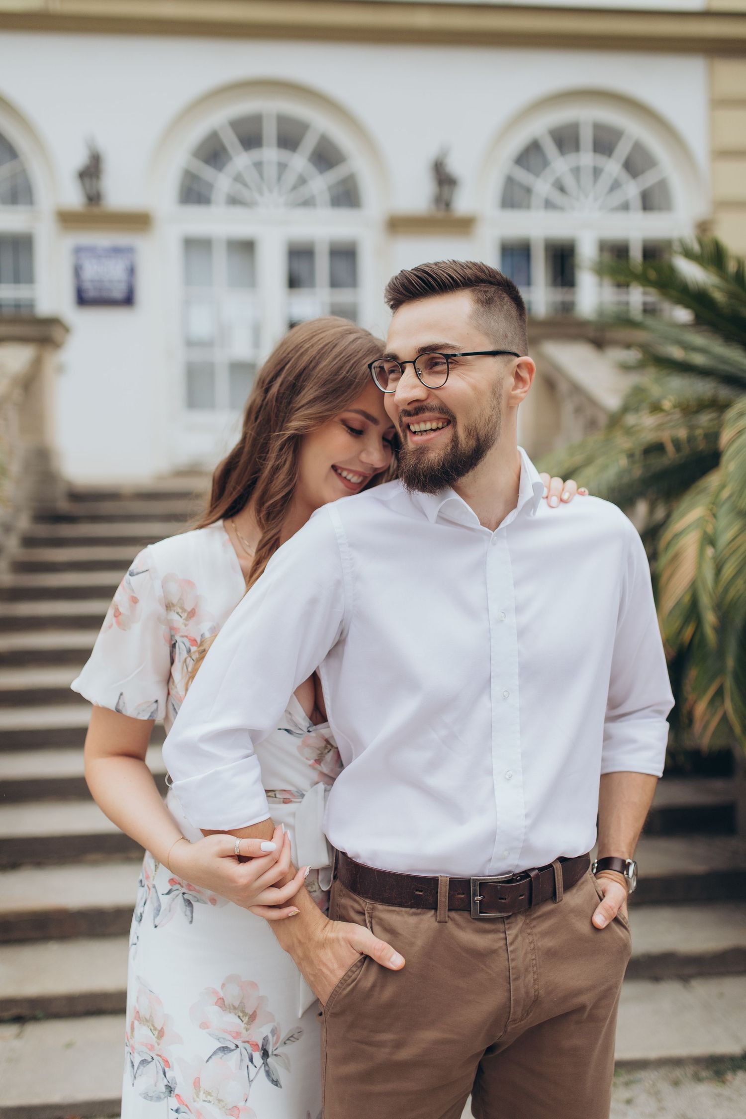 Intimate couple photo in front of a classic building with arched windows and grand staircase.