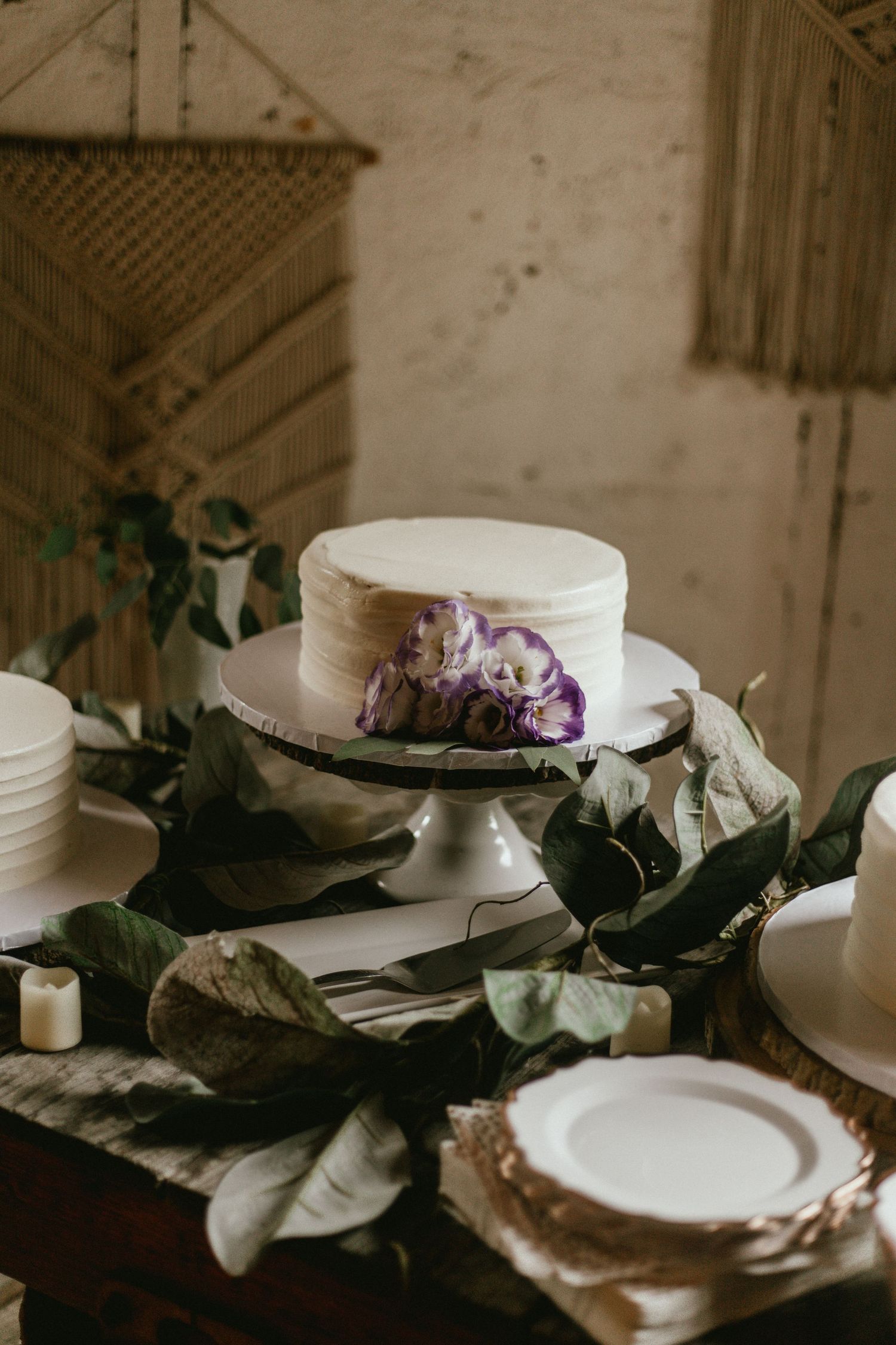 Elegant white wedding cake with purple floral accents on display with greenery decor.