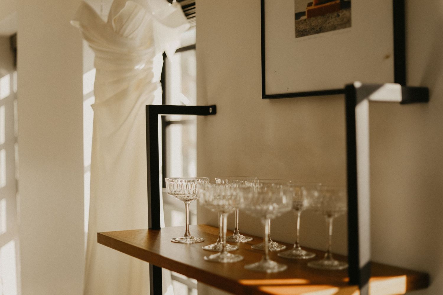 Row of empty champagne glasses on wooden shelf against white wall in elegant setting.