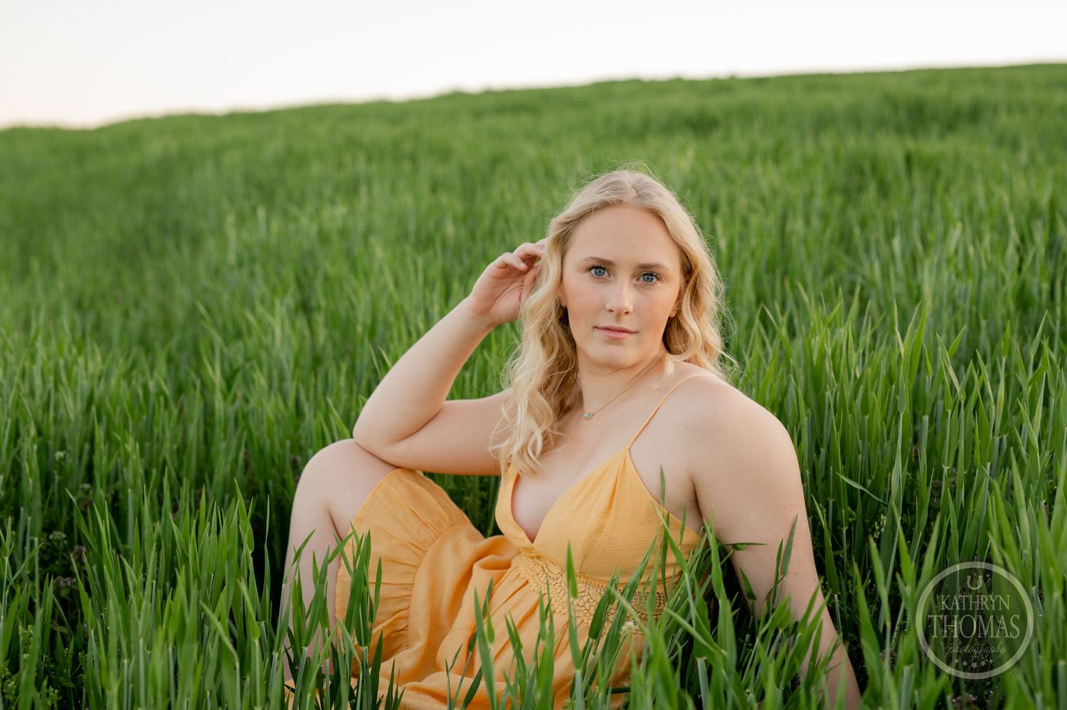 Portrait in yellow dress sitting among tall grass during sunset.