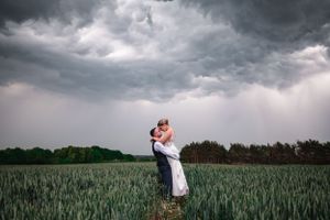 A couple embraces in a wheat field under dramatic stormy clouds during a romantic photoshoot. At Curradine Barns, Stoke.