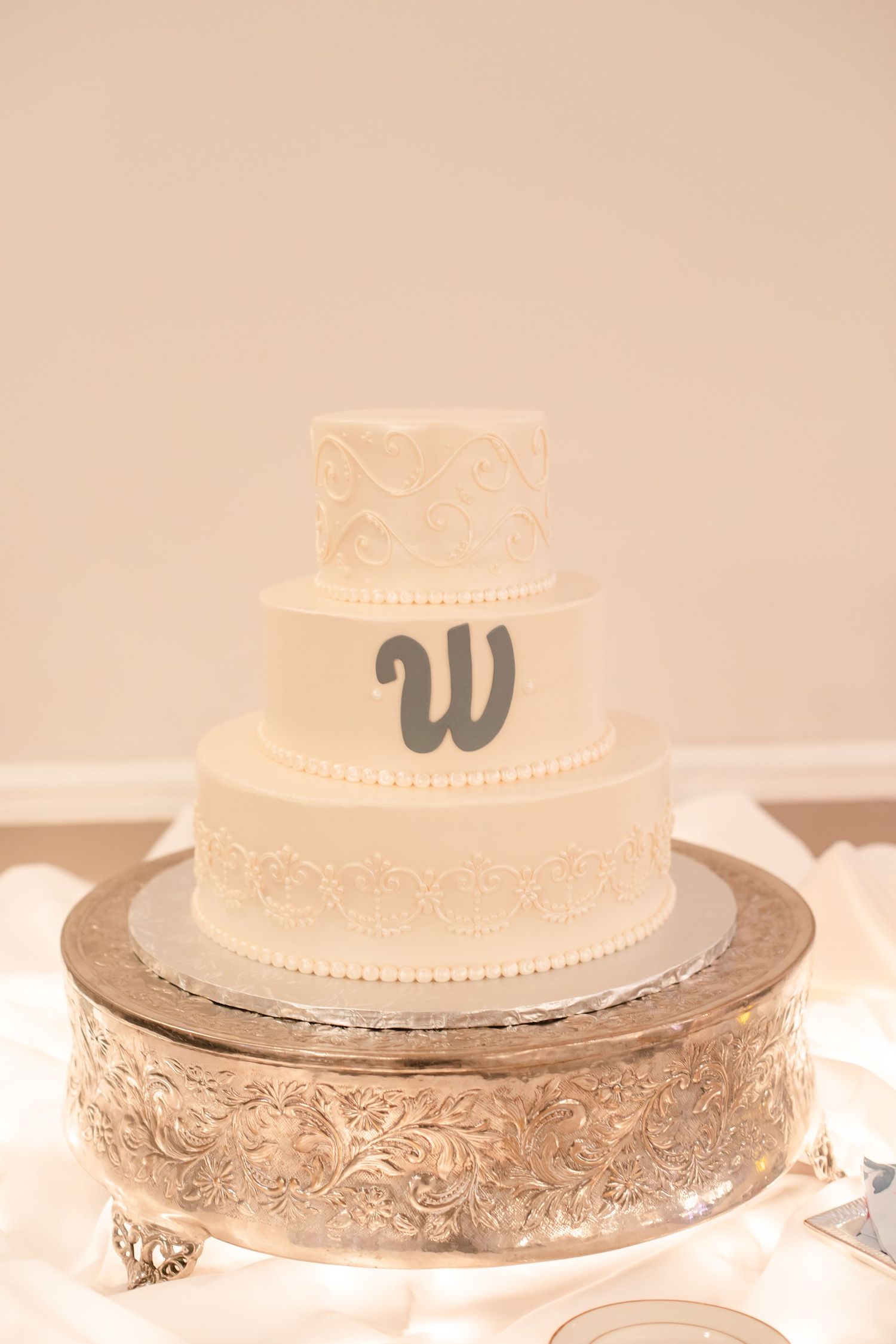 Classic white wedding cake with delicate lace pattern details displayed on an ornate silver cake stand.