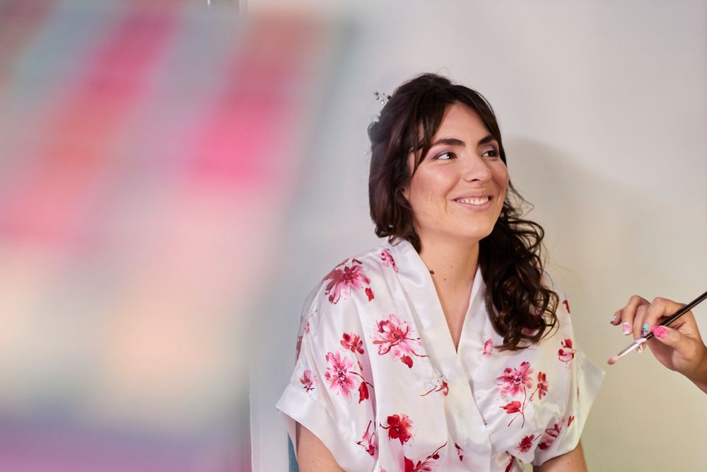 A person in a floral robe smiles while getting ready on their wedding day.