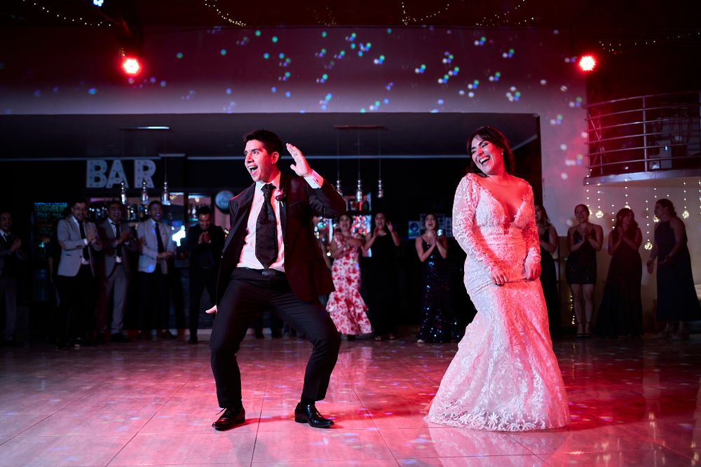 Wedding couple performs energetic first dance under colorful lights at reception.