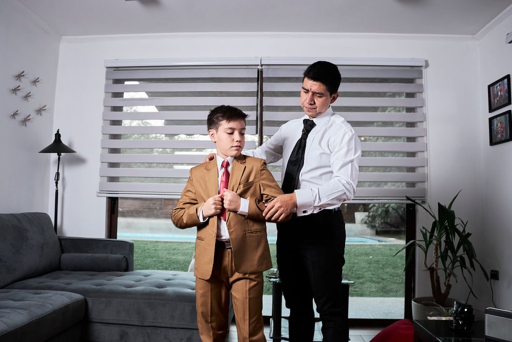 Two people help adjust formal attire in a modern living room setting.