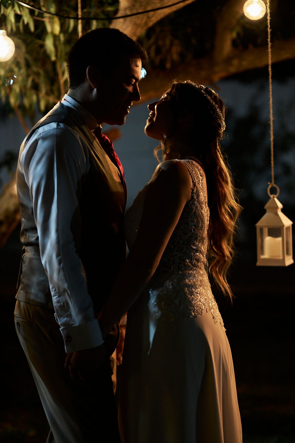 A romantic silhouette of a couple embracing under hanging lanterns at night.