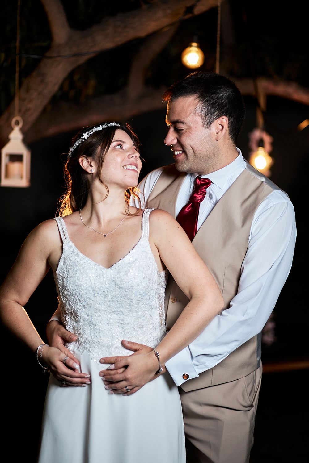 A couple shares an intimate moment during their wedding reception under rustic lighting and wooden beams.