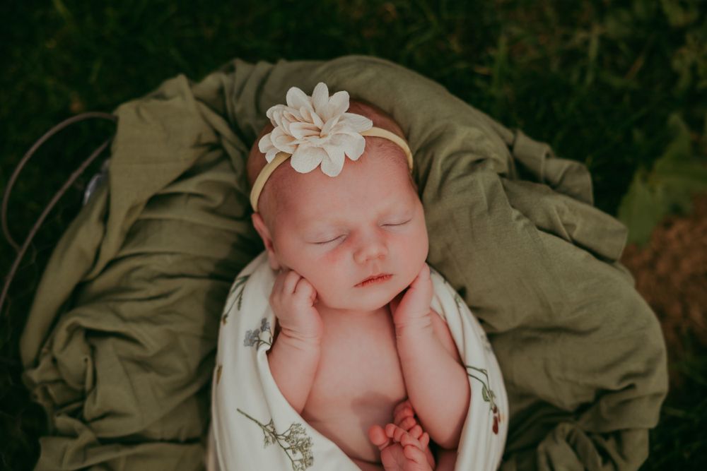 Newborn photography of sleeping baby on olive green blanket with white flower headband.