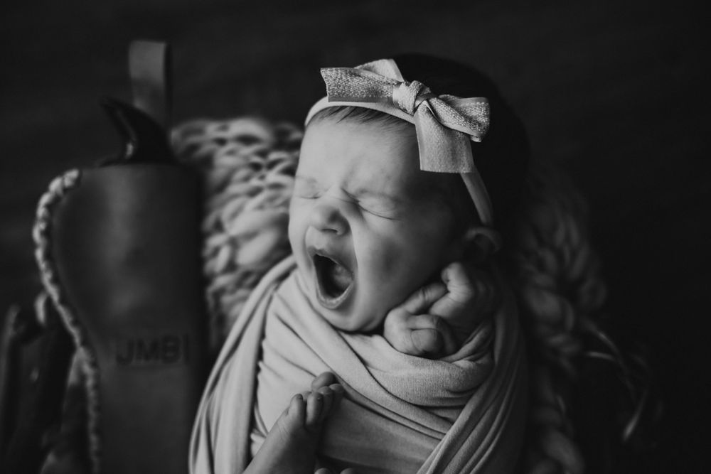 Black and white portrait of yawning newborn wearing bow headband.