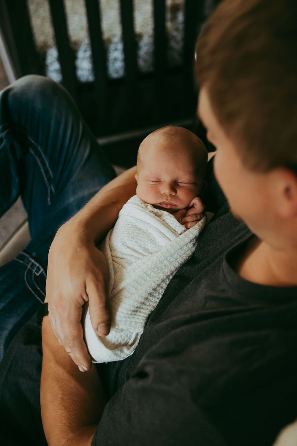 Intimate view of peaceful sleeping newborn wrapped in white swaddle being held.