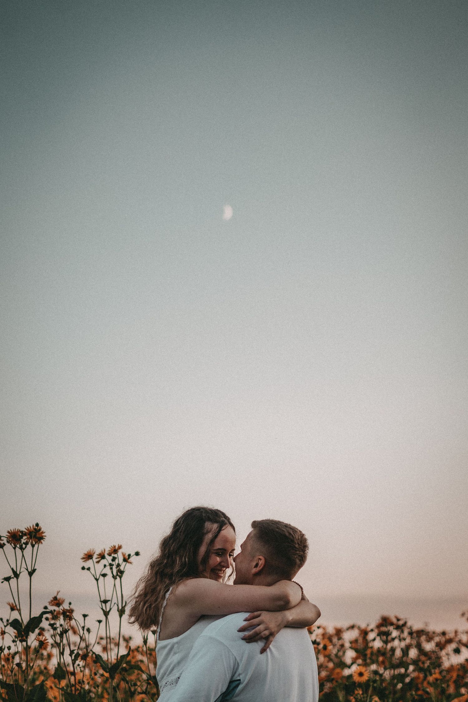Couple embracing in a flower field during sunset with dreamy atmosphere.