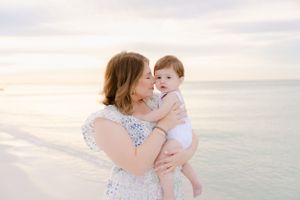 A tender moment between mother and baby on a beach at sunset.