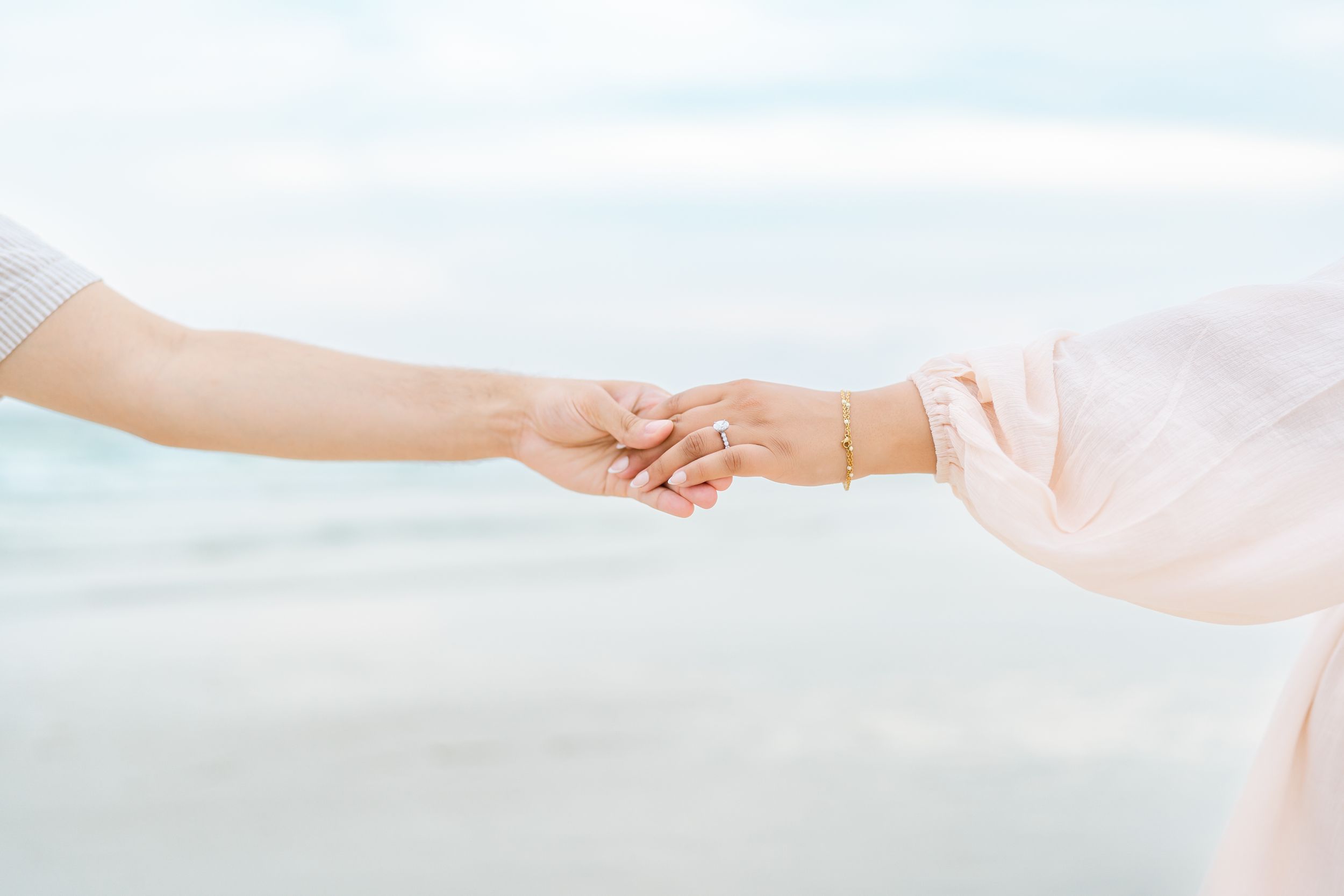Close-up of two hands reaching to hold each other against a dreamy beach backdrop.