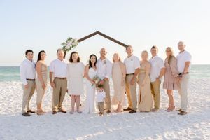 Wedding party in neutral colors posing together on beach with wooden arch.