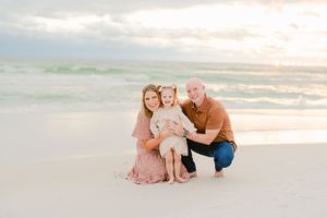 A family of four posing together on a sunny beach at sunset.