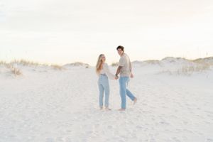 A couple walking together on pristine white sand dunes at sunset.