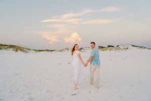Couple holding hands while standing on white sand dunes during sunset.