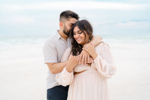 Romantic couple embracing on a white sand beach at sunset wearing light colored clothing.