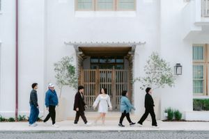 Group of people walking past elegant wooden doors of white Mediterranean building.