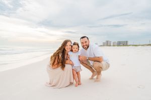 Family in light colored clothes sharing joyful moment on white sandy beach.