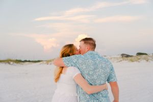 Couple embracing on white sand beach during sunset.