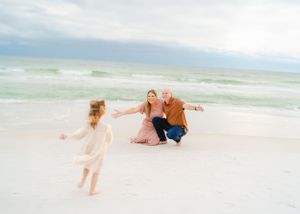 A family playing together on a white sandy beach near the ocean.