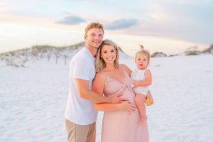 Family embracing on white sandy beach during golden hour sunset.