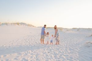 A family walks together on pristine white sand dunes at sunset creating soft footprints in their path.