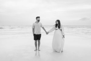 Black and white photo of couple holding hands while walking on an empty beach.