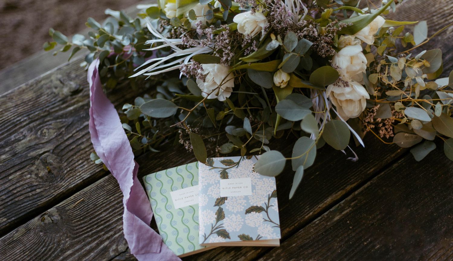 Delicate floral arrangements with white roses and greenery displayed on rustic wooden surfaces.