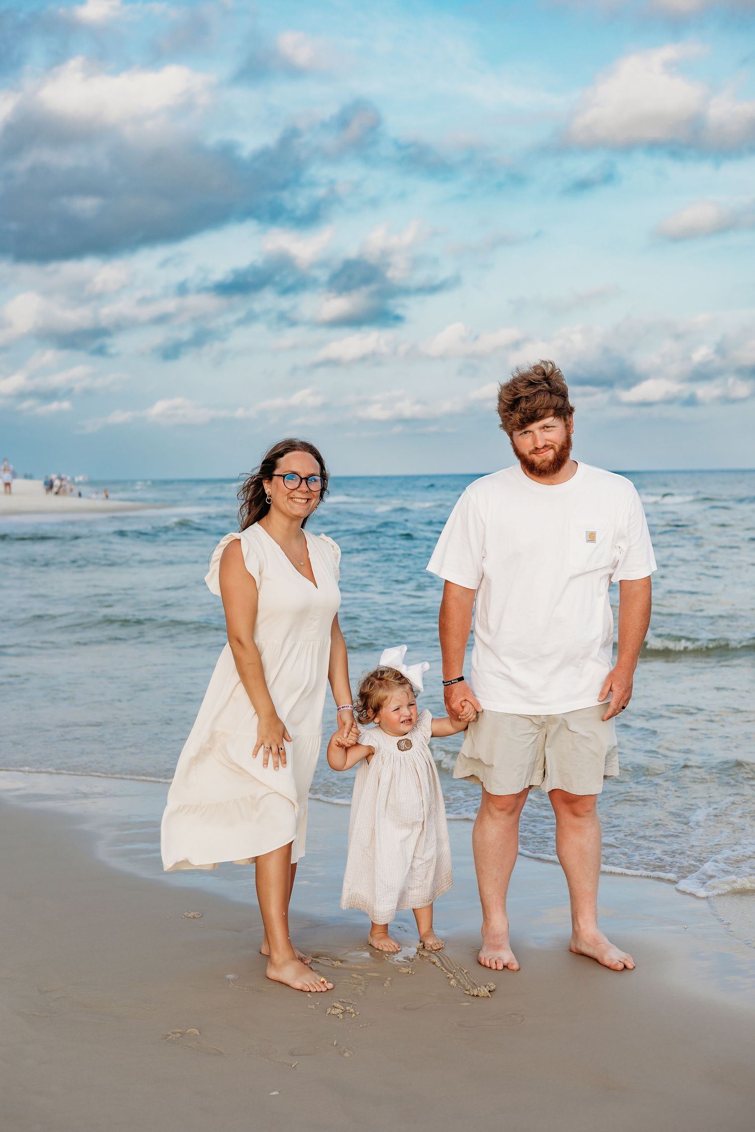 Family walking together along a scenic beach shoreline wearing coordinated white outfits.