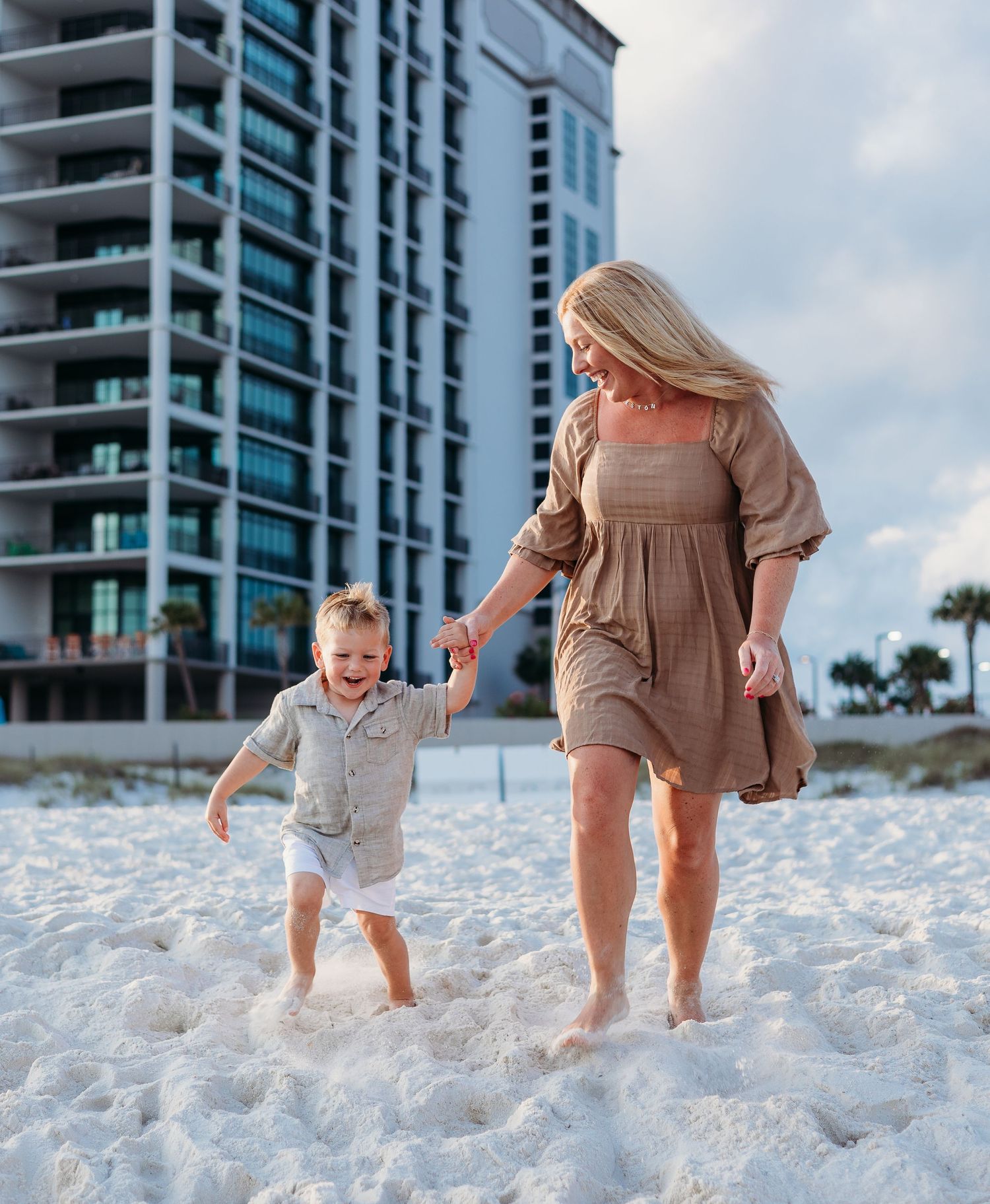 Parent and child playing in pristine white sand near beachfront condominiums.