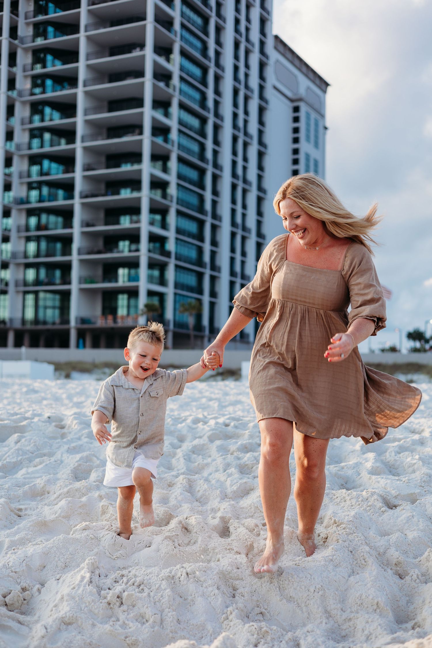 Joyful moments captured running and playing in white sandy beach with high-rise building backdrop.