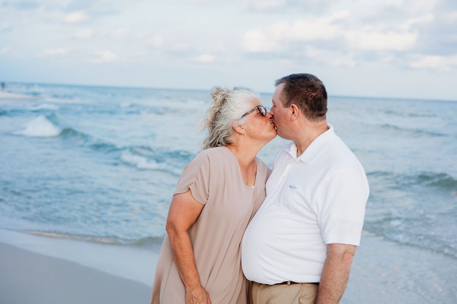 Romantic beach photoshoot with gentle waves and cloudy sky backdrop.